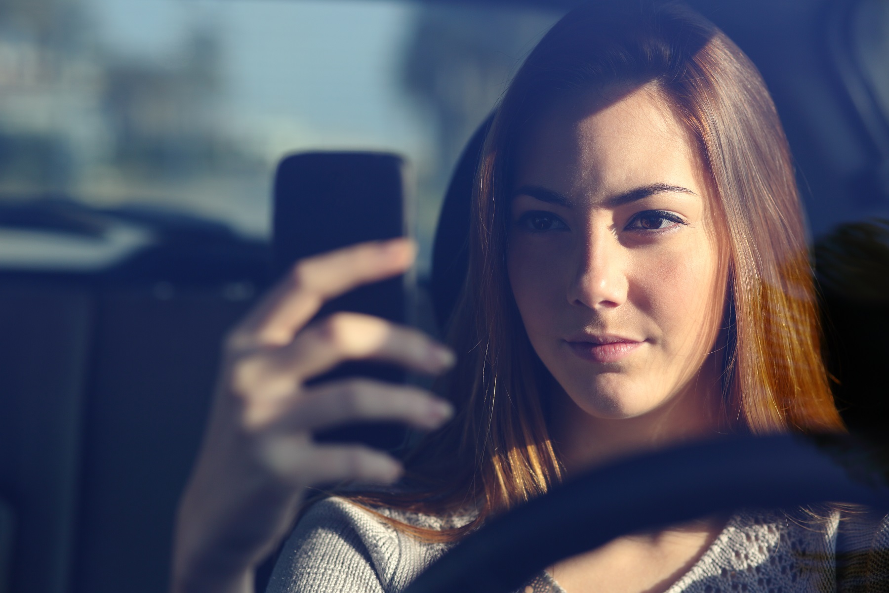 Front view of a woman driving a car and typing on a smart phone